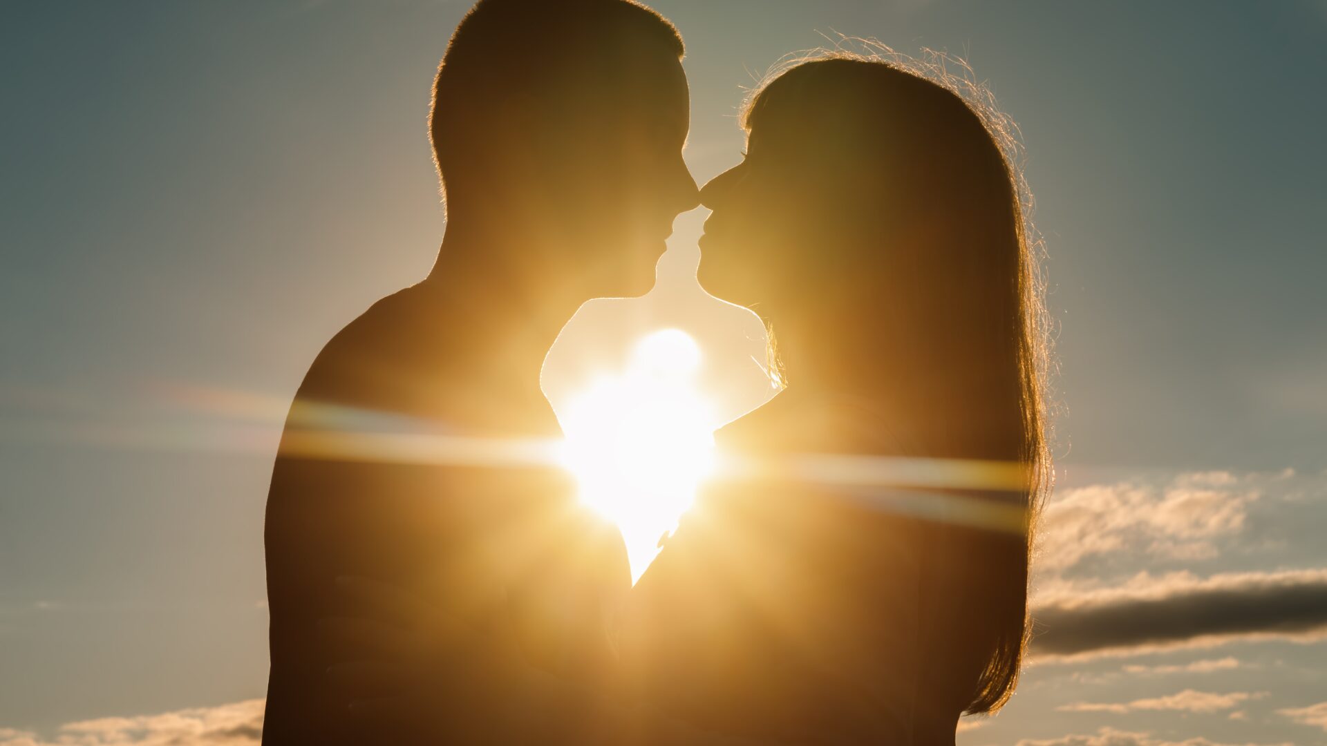男性と女性が口づけしようとする向こう側から夕陽が二人を照らしている