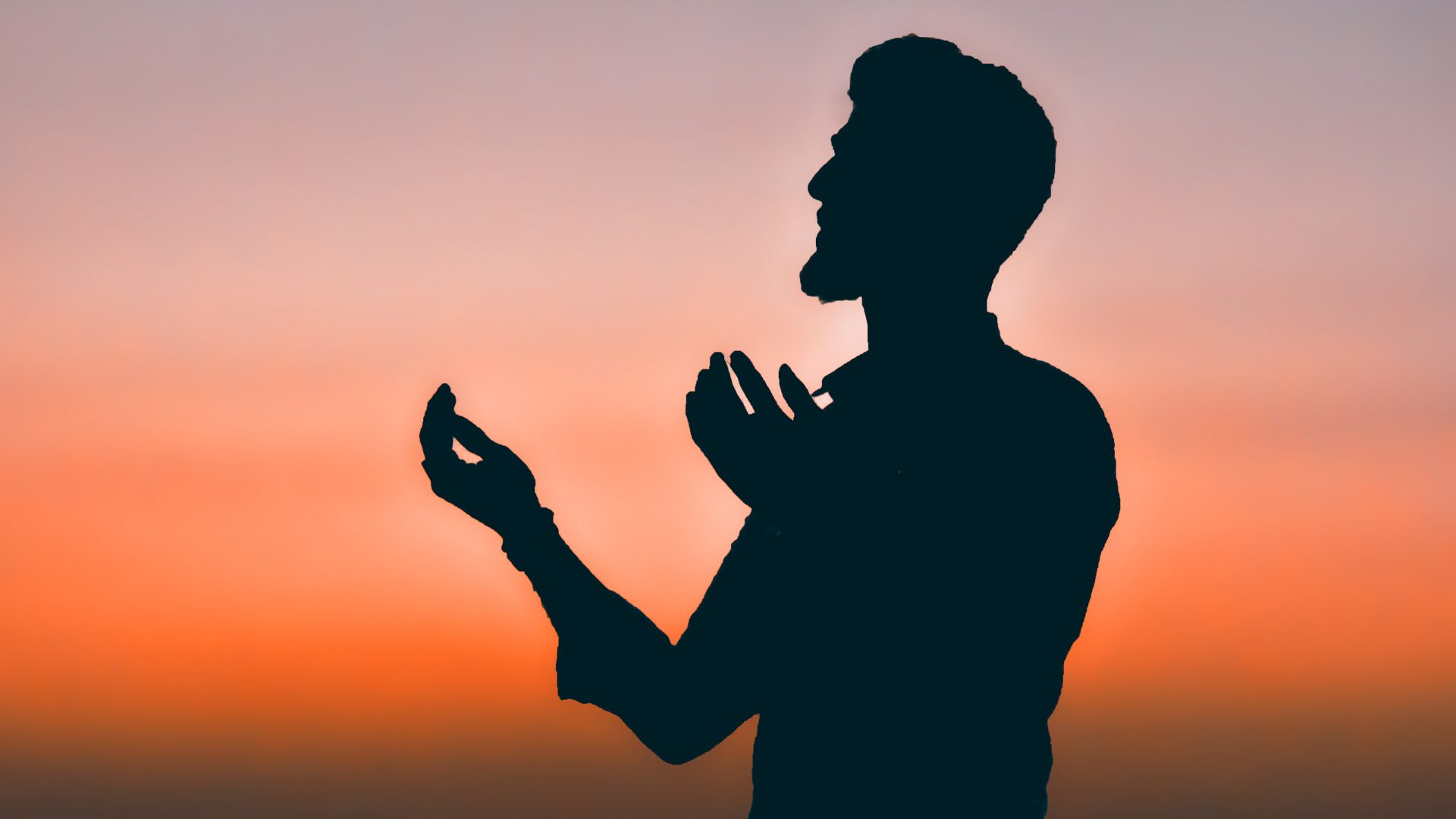 両手を広げて祈っている男性の向こう側に綺麗な夕焼けが広がっている