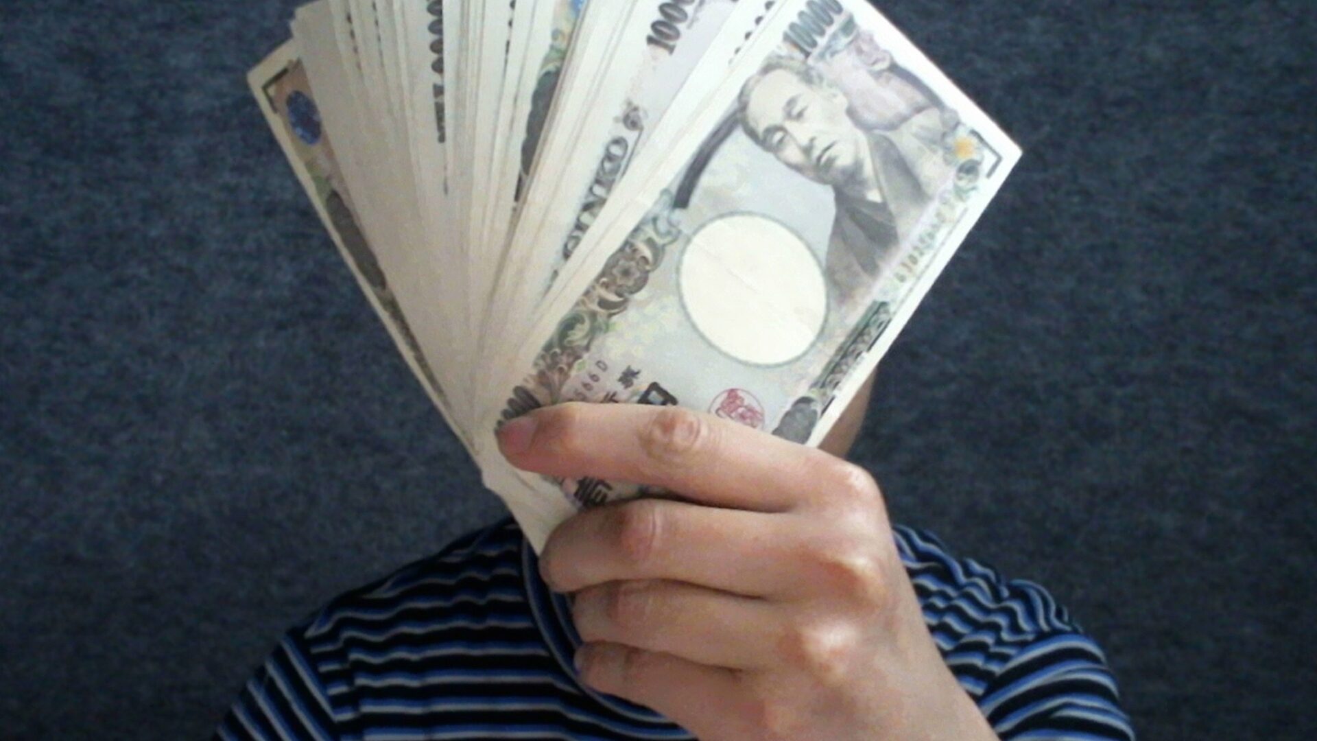 顔の前で数枚の一万円札を扇形に広げている